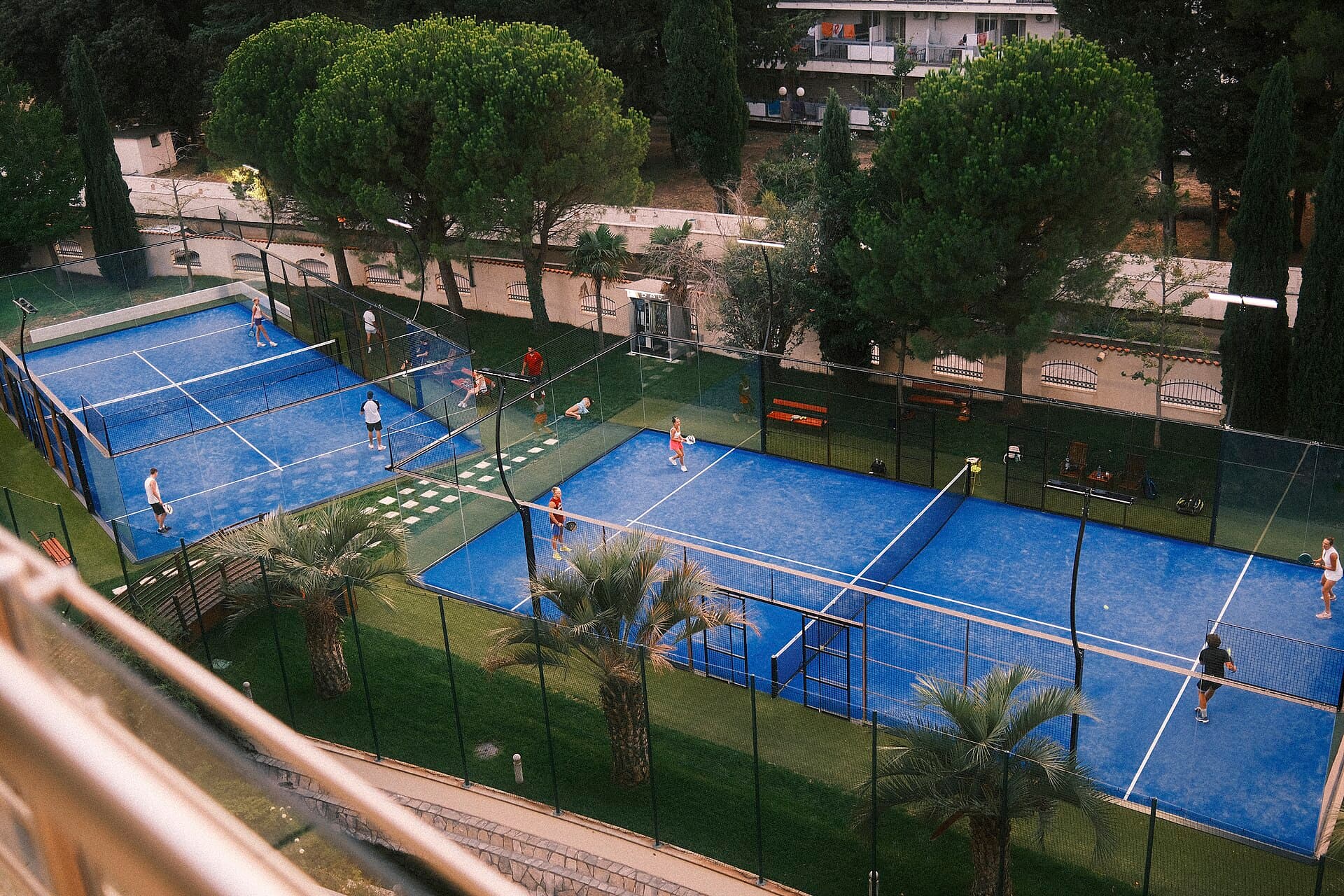 Padel players on outdoor courts surrounded by greenery